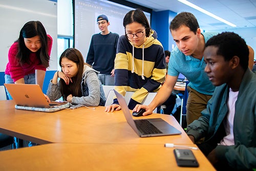 students in a classroom gathered around laptops