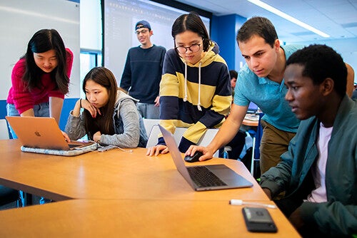 students in a classroom gathered around laptops
