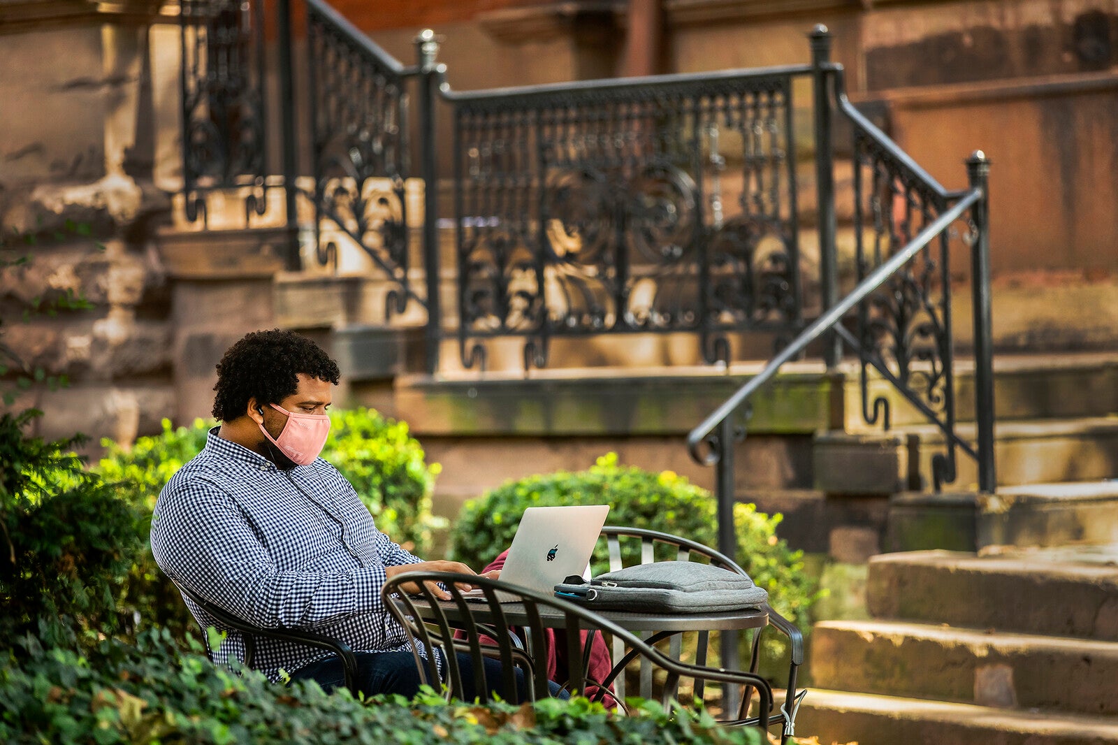 student sitting on locust walk on a laptop with mask