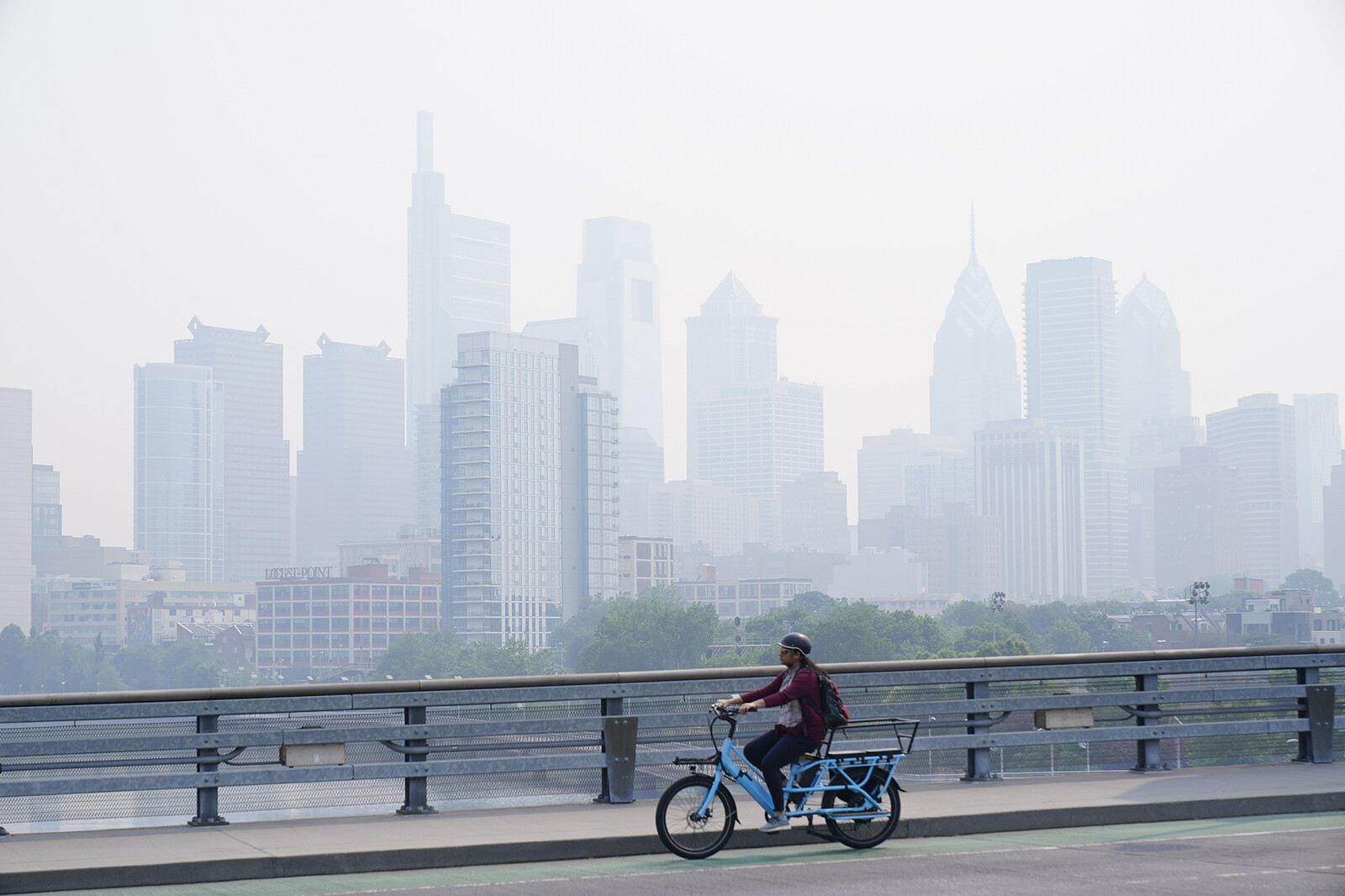 a cyclist rides a bike in front of a smoky philly skyline