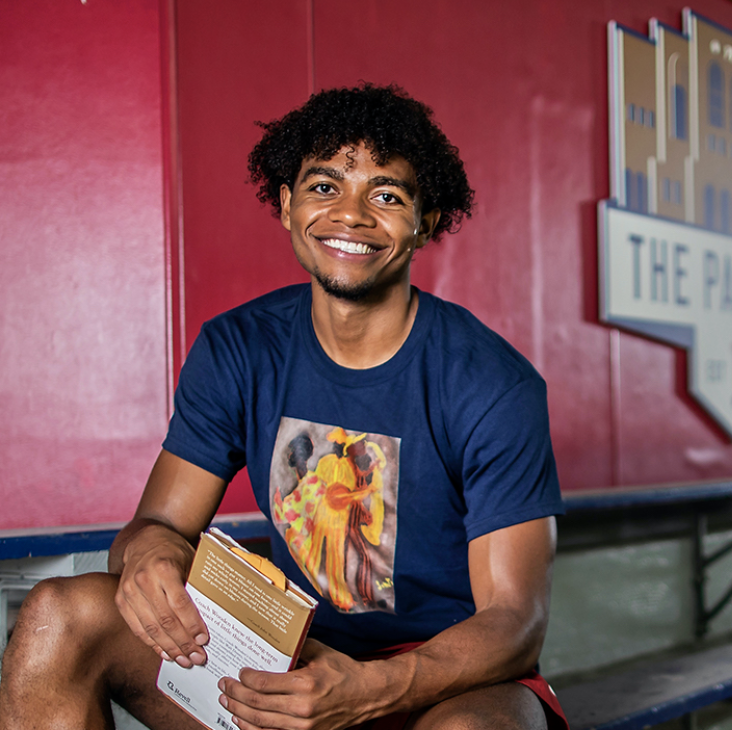 Lucas Monroe sitting on bleacher with book and smiling at camera