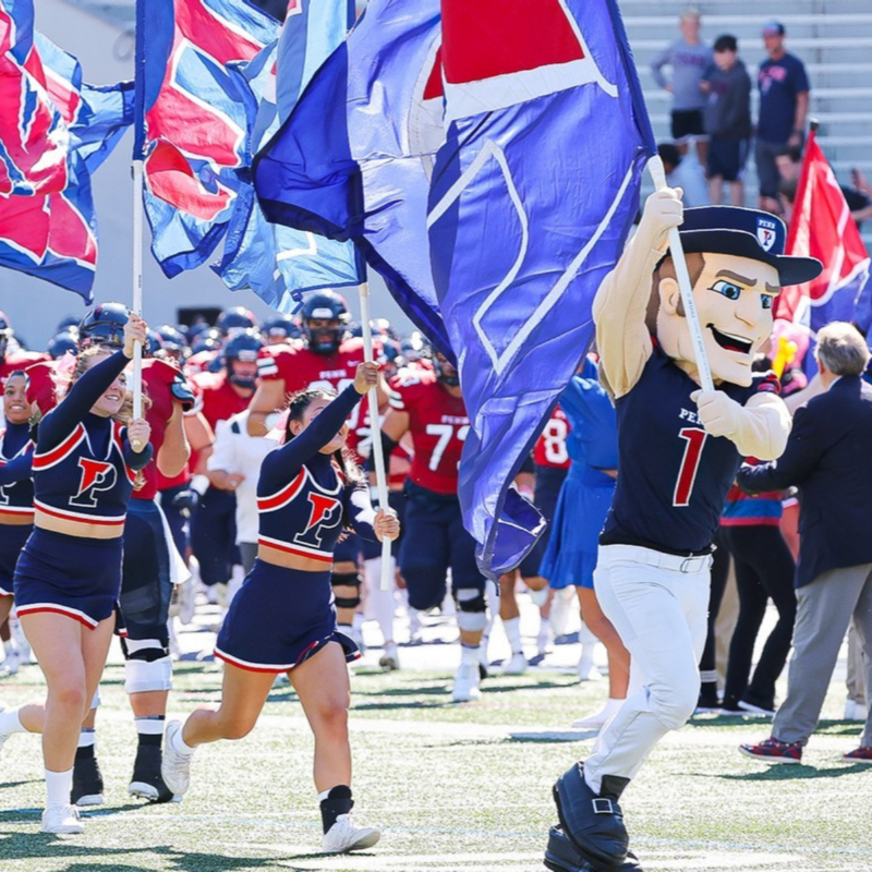 Penn Mascot and cheerleaders running onto the field holding UPenn Flags