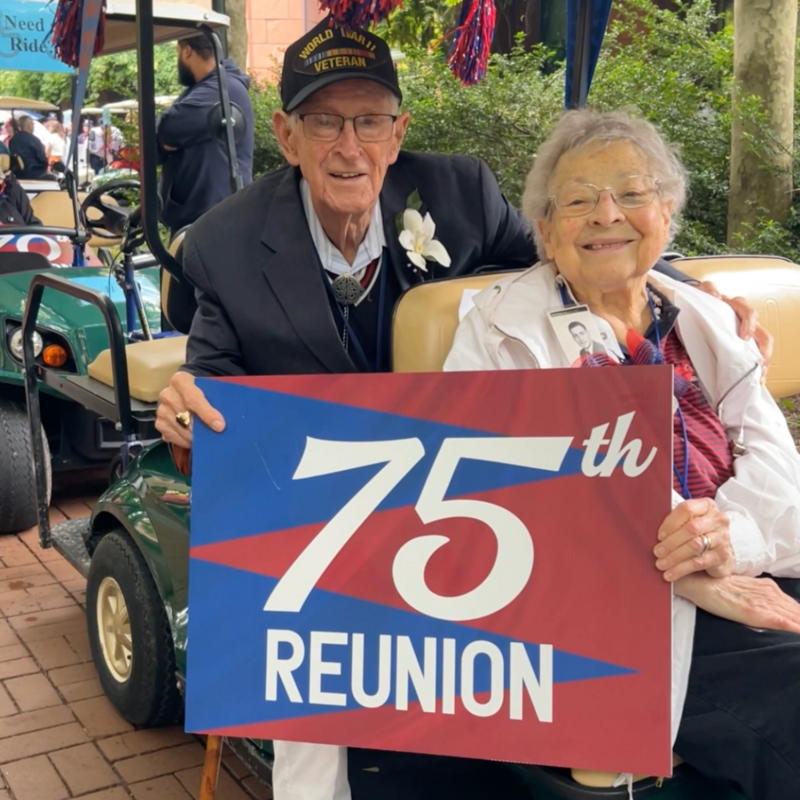 Two older Penn Alumni holding a sign that says "75th Reunion"