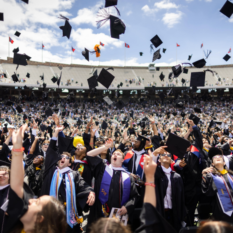 Graduating students all through their caps in the air in unison celebrating their graduation.