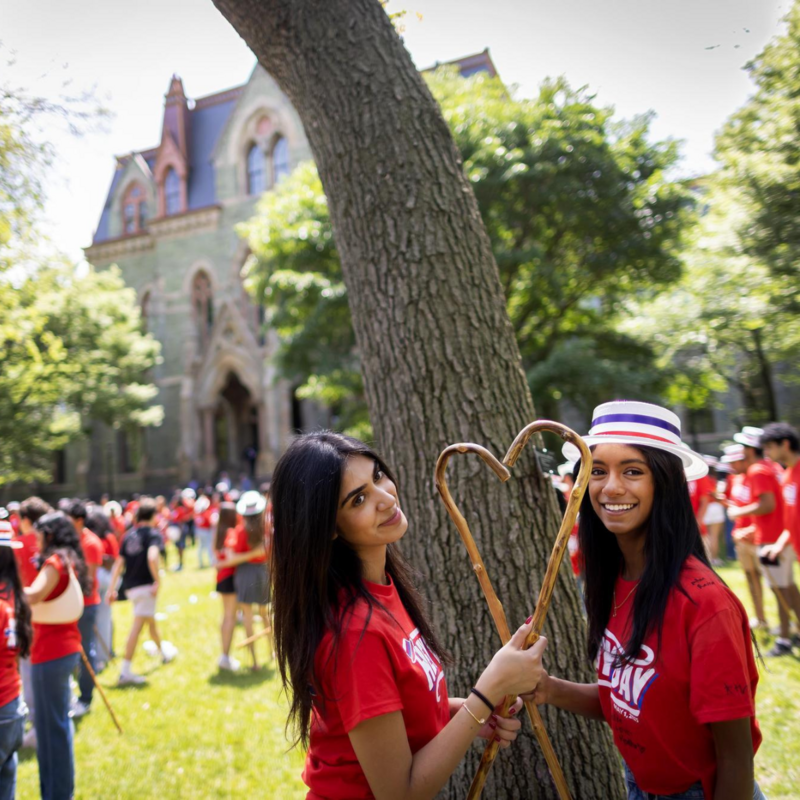 Two students wearing matching red Hey Day shirts hold two canes in the shape of a heart as the pose for a photo.