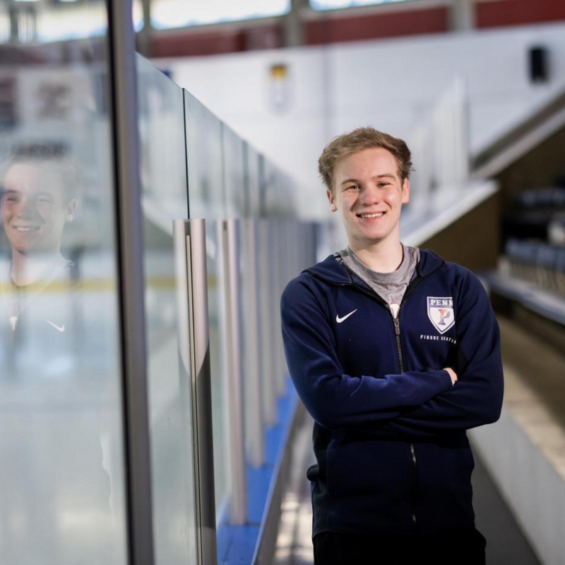 Nick Bausenwein standing next to the glass at the Penn Ice Rink with his arms folded and smiling.