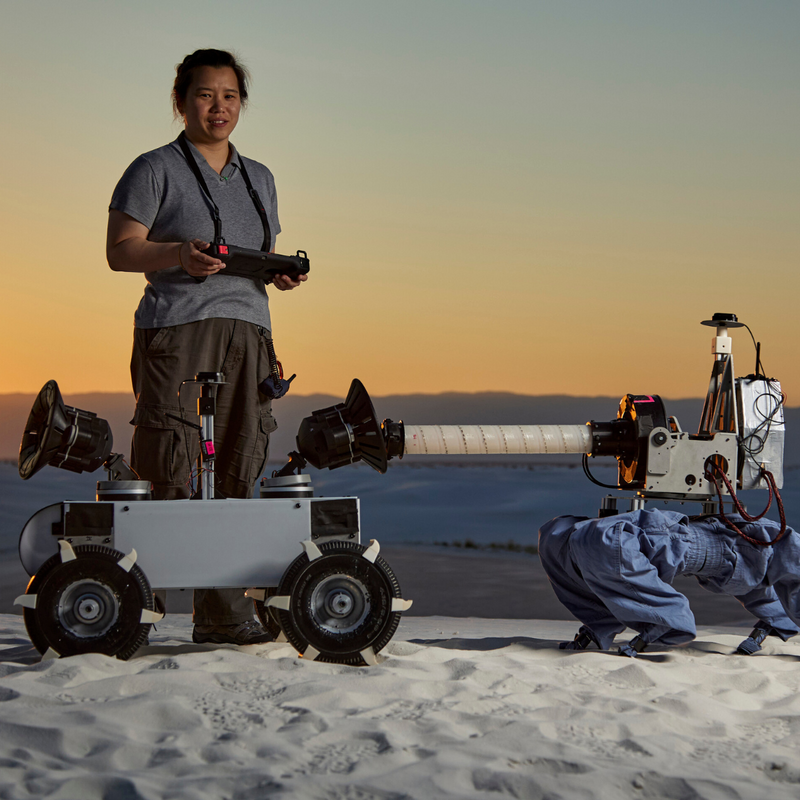Member of the Sung Robotics Lab at Penn Engineering standing with a wheeled and legged robot system in the sandy dunes of New Mexico.